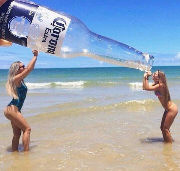 Girls at the beach holding up what looks like a giant beer bottle which is just the photographer holding up his Corona with the girls positioning their arms perfectly.
