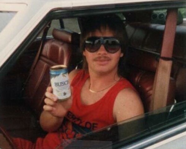 Man in a tank top with 80's glasses drinking a Busch beer.