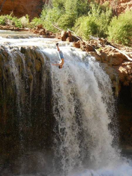 Man doing an awesome backflip off a waterfall.