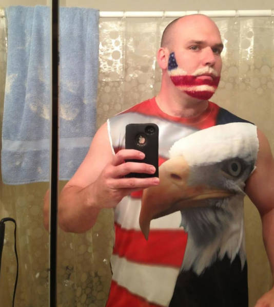 Man wearing a USA flag shirt with a huge bald eagle on it also has an American flag painted beard.