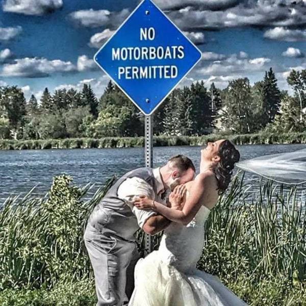 Groom motorboating his bride next to sign that says No Motorboats Permitted