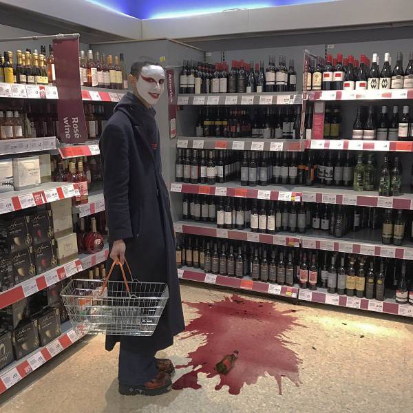 Man with strange mask at the liquor store with a broken bottle of red wine on the floor.