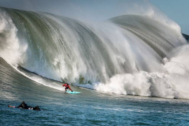 Awesome picture of a surfer with some major wave breaking behind him.