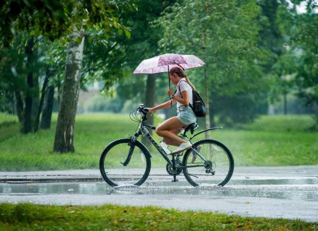 Cute girl riding her bike in the rain while holding an umbrella.
