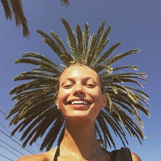 woman posing for selfie that looks like the palm tree behind her is her hat