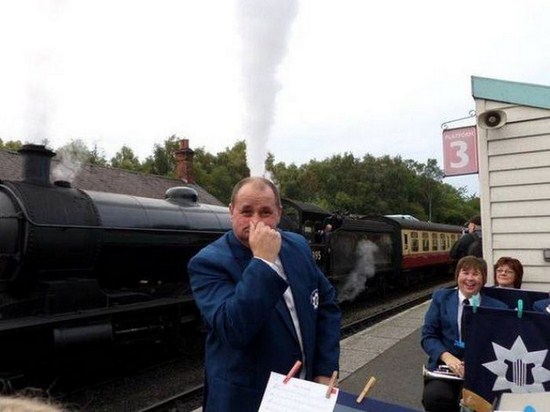 Man blowing nose with steam locomotive releasing white steam right behind his head.