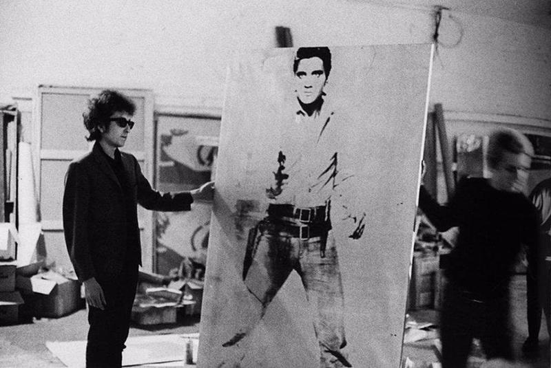 Here's a photo of Bob Dylan taken back in 1965. Apparently, he once traded an original Andy Warhol piece, for a couch. Here he is with a significant Warhol artwork, titled "Elvis with a Gun"– It's said Dylan took to tossing darts at it.