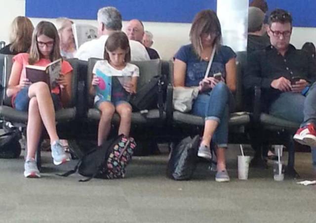 family at the airport and the parents are on their phones and the kids are reading books
