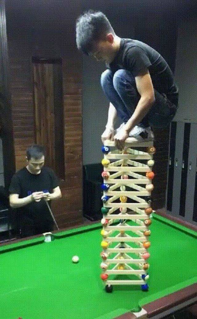 kid standing on top of stacked balls and pool triangles as setup for a trick-shot to replace the bottom 8 ball with some force
