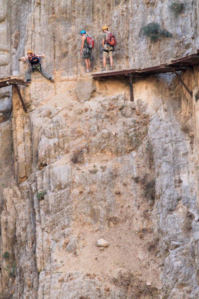 bridge along a cliff that is a bit missing as climbers make their way across