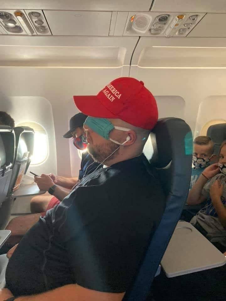 guy wearing a face mask over his eyes as a sleep mask and a make america great again MAGA hat on a plane