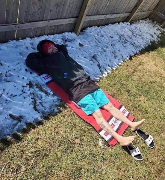guy lying in snow in the shade and wearing swim shorts on the bottom in the sun