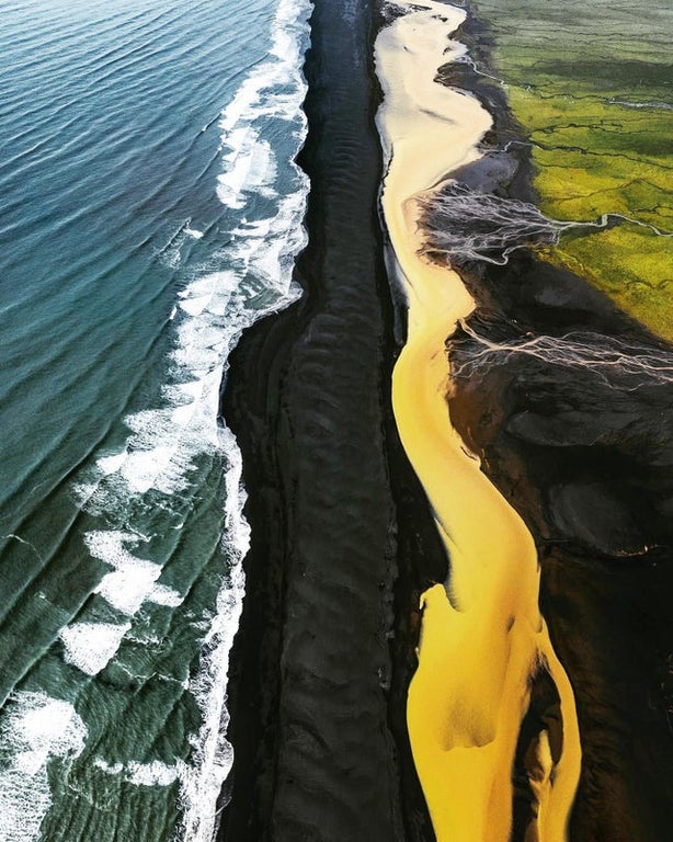 green fields yellow river black beach and blue sea in iceland