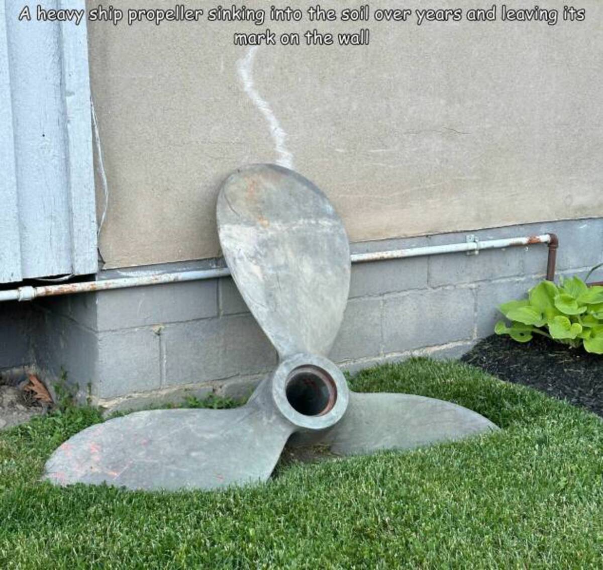 grass - A heavy ship propeller sinking into the soil over years and leaving its mark on the wall