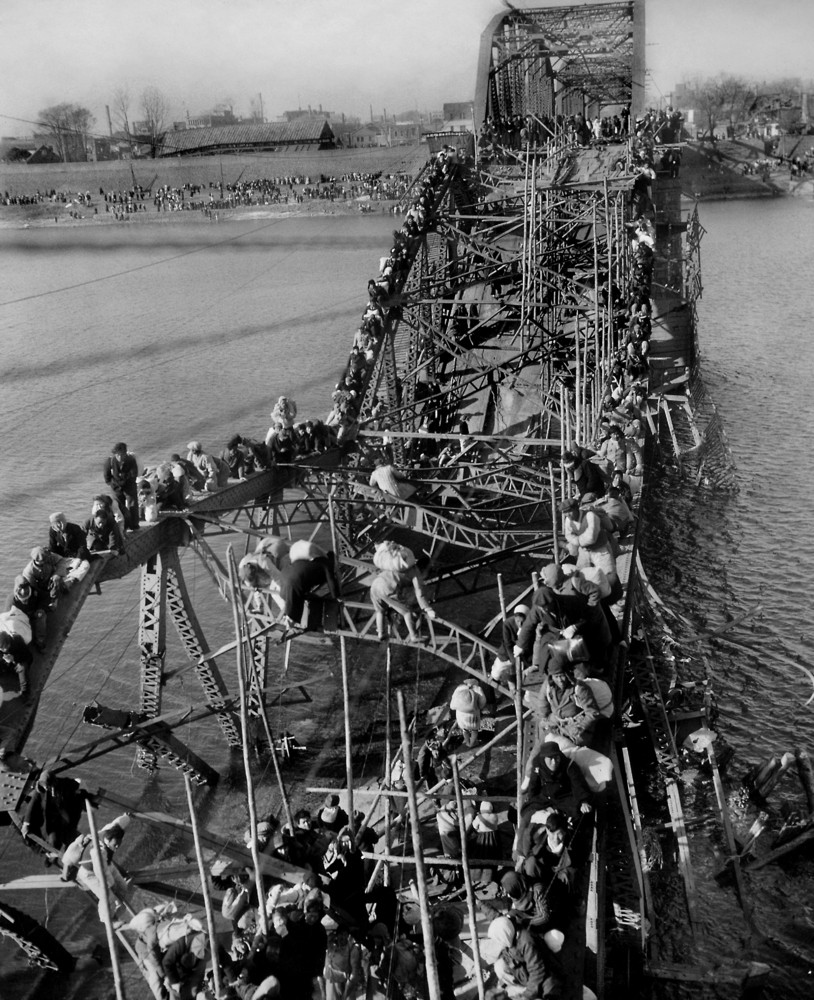 Residents from Pyongyang, North Korea, and refugees from other areas crawl perilously over shattered girders of the city's bridge on December 4,1950
