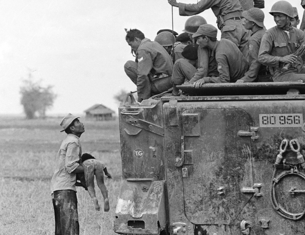 A father holds the body of his child as South Vietnamese Army Rangers look down from their armored vehicle March 19,1964