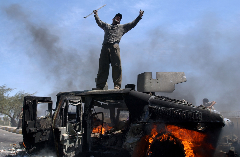 An Iraqi man celebrates atop of a burning U.S. Army Humvee in the northern part of Baghdad, Iraq, Monday, April 26, 2004.