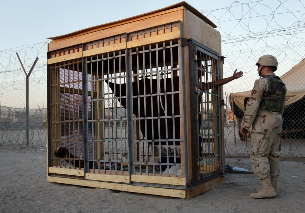 A detainee in an outdoor solitary confinement cell talks with a military policeman at the Abu Ghraib prison on the outskirts of Baghdad, Iraq, June 22,2004