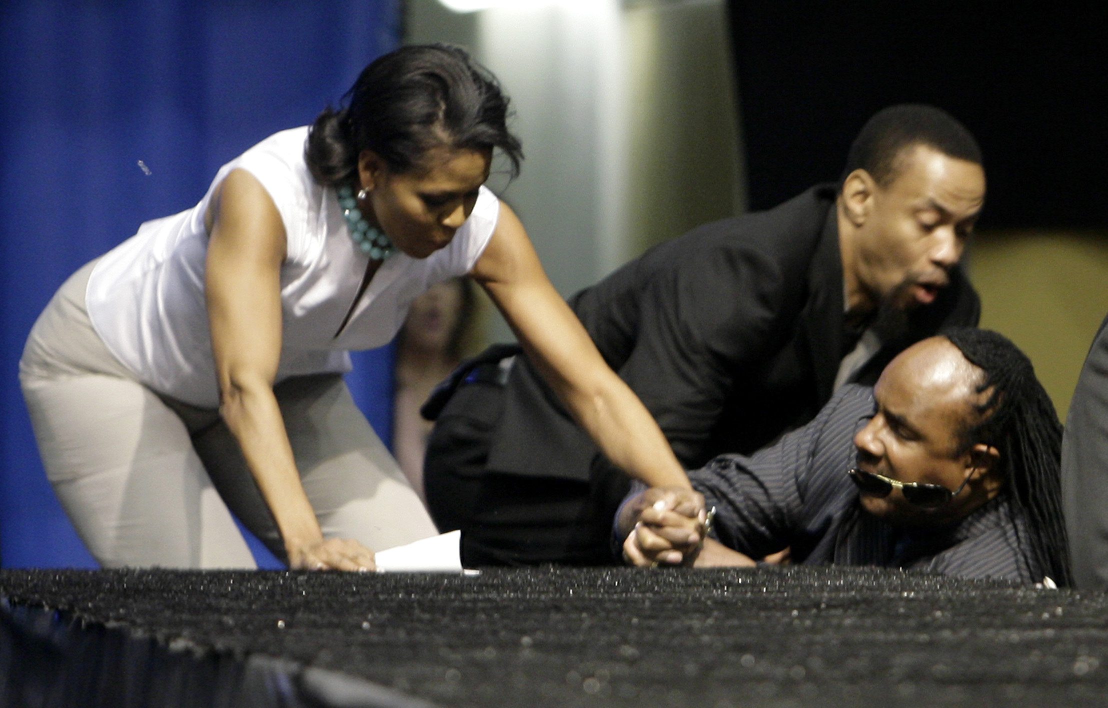 Michelle Obama and singer Stevie Wonder fall as they go up steps to the stage at UCLA's Pauley Pavilion
