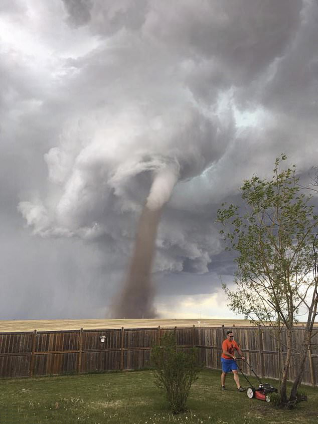 A man mows his lawn without a care in the world… despite a tornado swirling menacingly behind him