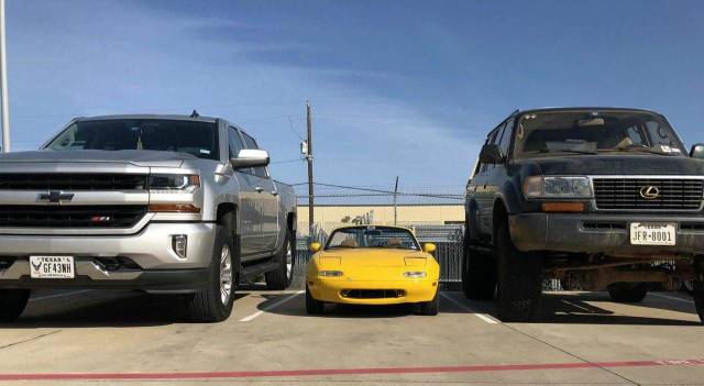 random photo of little yellow mazda miata surrounded by a large Chev and Lexus SUV