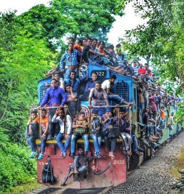 random photo of a train that is way beyond it's passenger capacity with people on the front, sides and top