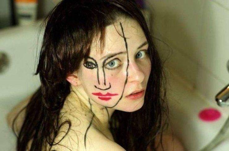 Cursed image of Woman sitting in a bath looking at the camera with a face drawn on the side of her face by sebastian bieniek