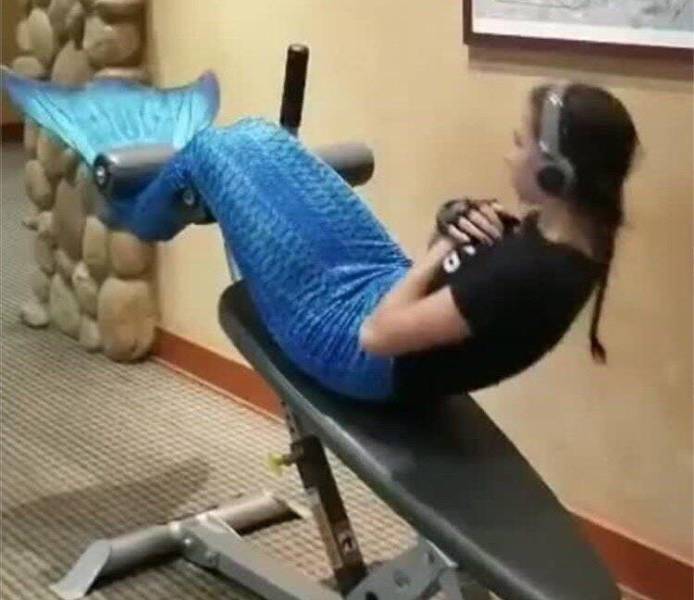 Cursed image of Woman doing sit ups on a sit up machine while wearing a mermaid costume