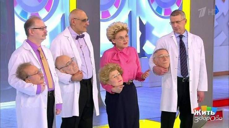 Cursed image of 3 scientists in labcoats and a tv host all holding fake heads that look like them