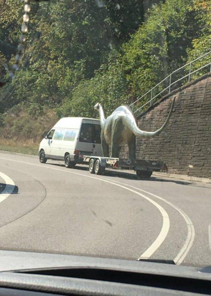 truck carrying a dinosaur statue on the road