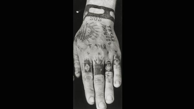 The tattoo on his pointer finger means his parents died while he was in prison. middle finger: he served his full sentence, without parole. Ring Finger: The upside-down spade means he was convicted for hooliganism.