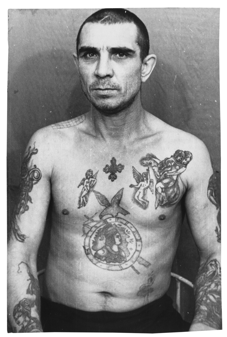 The cross in the center of his chest shows allegiance to the thieves, but its small size shows that he holds very little power among them. Tattoos of saints and angels are commonly used to show that the prisoner is not mired in betrayal.