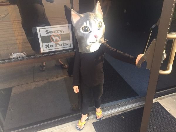 Kid wearing a cat mask next to a sign that says 'sorry no pets' r4p9k7ve