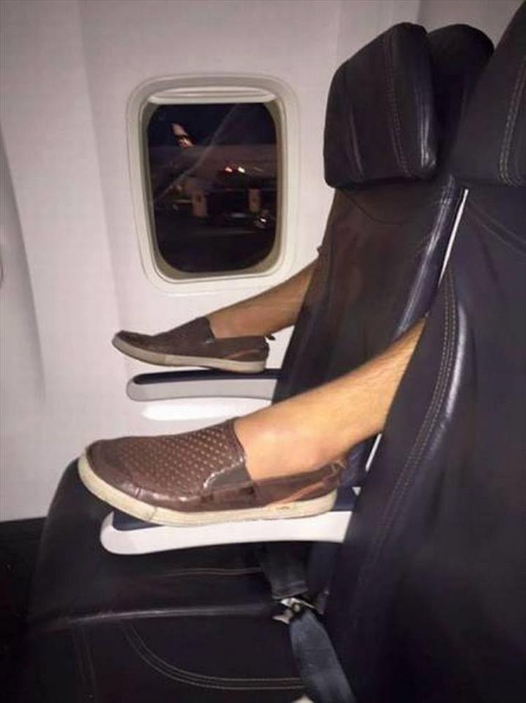 Airplane seat with the feet of the person behind it sticking through in a very rude way.