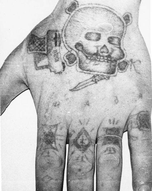 Text across the knuckes reads NADYA (womans name). The ‘ring’ on the forefinger stands for ‘Rely on no one but yourself’, a ‘patsan’ one of the most privileged inmates VTK. Middle finger ‘the thieves cross’ of a pickpocket. Third finger: ‘I served my time in full’, ‘From start to finish’, ‘Went without parole’, the prisoner served his complete sentence with no remission for working with the system. Little finger ‘The dark life’ the bearer spent a lot of time in a punishment cell. The skull and crossbones, gun, knife and letter ‘K’[iller] denote a murderer.