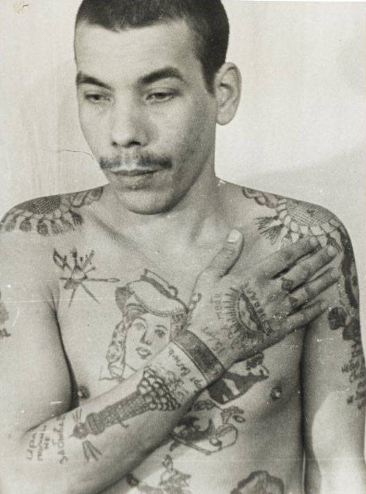 This man is a Muslim; his features also indicate he is not Russian. Text on the arm reads ‘Remember me, don’t forget me’ and ‘I waited 15 years for you.’ On his stomach (left) is a religious building with a crescent moon. He is not an authoritative thief, but has tried to imitate them with his tattoos to increase his standing within the prison. The lighthouse on his right arm denotes a pursuit of freedom. Each wrist manacle indicates a sentence of more than five years in prison.