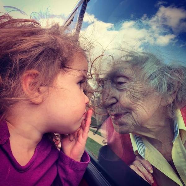 A little girl is sending fluffy kisses to her beloved great-grandma through the window.