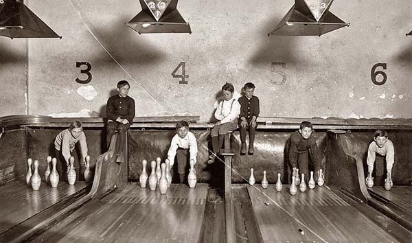 Pin boys set up bowling pins while people play games - 1914.