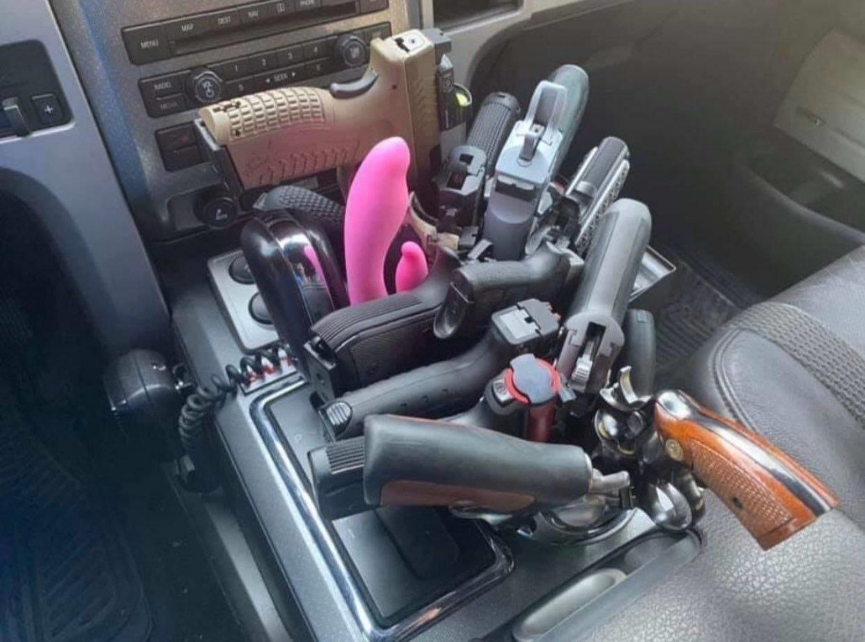 dildo pink sex toy in the car next to a bunch of guns