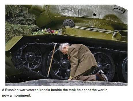 A Russian War veteran kneels beside the tank he spent the war in, now a monument.