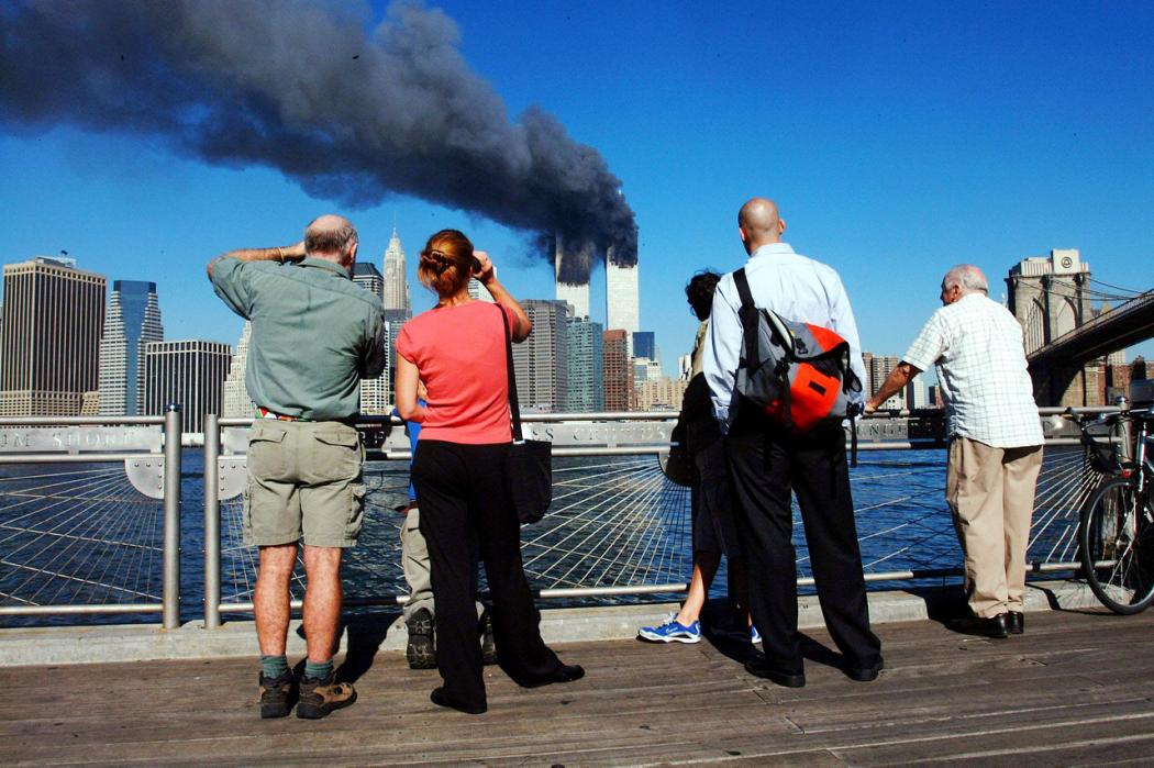 Pedestrians on the waterfront in Brooklyn look across the East River to the burning World Trade Center towers on Sept. 11, 2001.