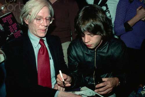 Mick Jagger signs an autograph for Andy Warhol.