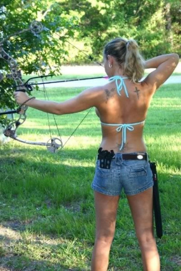 Girl in bikini top about to fire an bow and arrow.