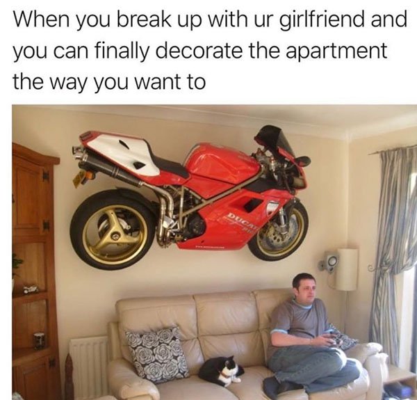 Man in living room with cat and motorcycle mounted overhead and caption about when you break up with your girlfriend and you can finally decorate the apartment the way you want to.