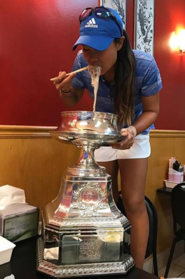 Woman eating something cheesy from a large trophy.