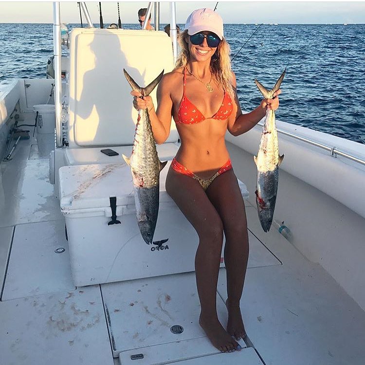 Cute girl on a boat holding 2 fish she caught.