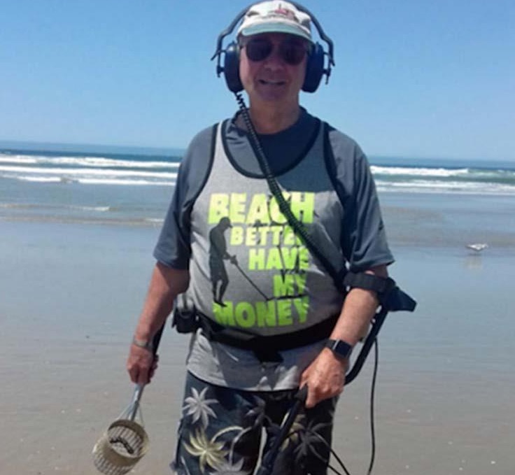 Funny pic of man on the beach with funny shirt about why he has a metal detector.
