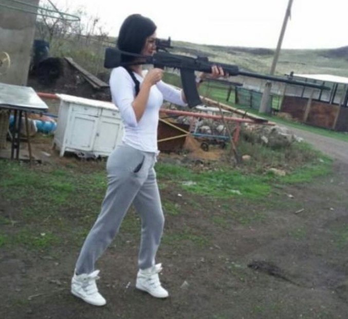 Girl holding assault rifle in a way that will hurt her eye if she actually fires it that way.