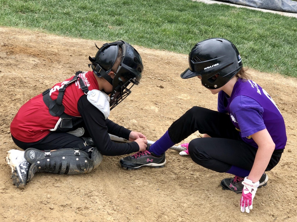 This youth softball player stopping the game so she can tie her opponent’s shoe