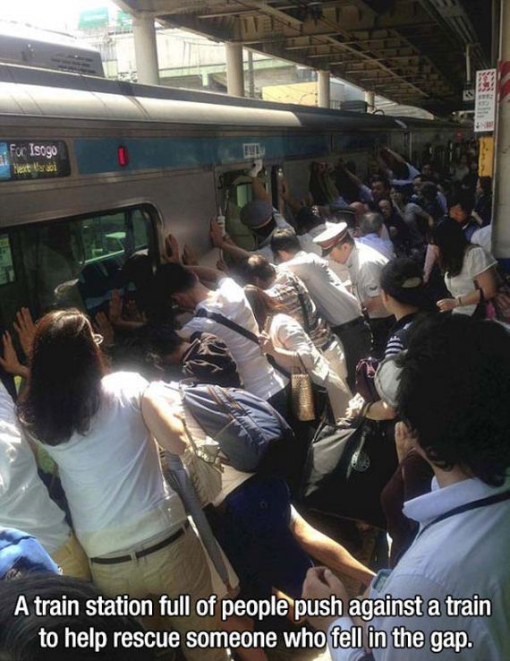 for Isogo A train station full of people push against a train to help rescue someone who fell in the gap.